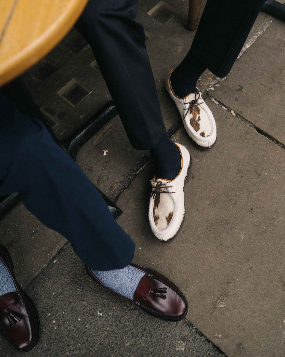 Two pairs of feet wearing different styles of shoes on a sidewalk.